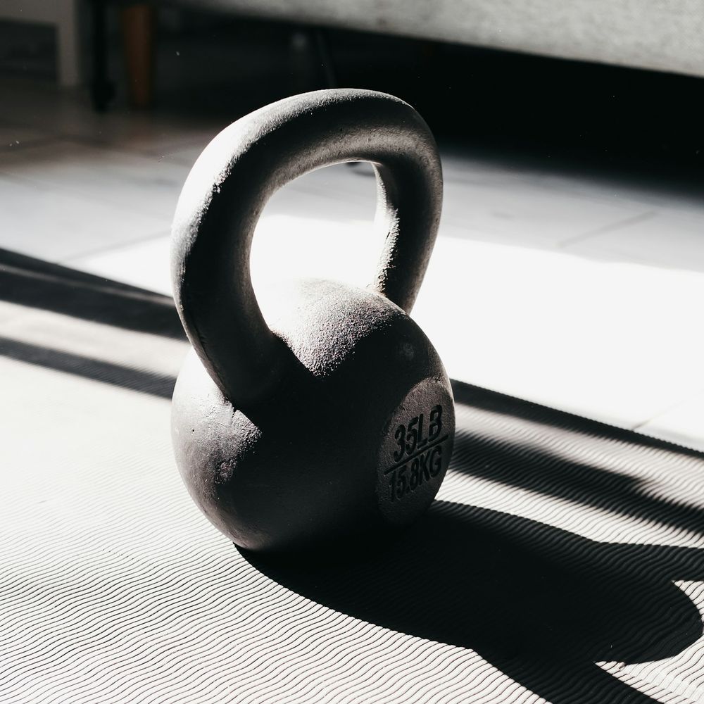 Black kettlebell standing on a light mat casting a long shadow