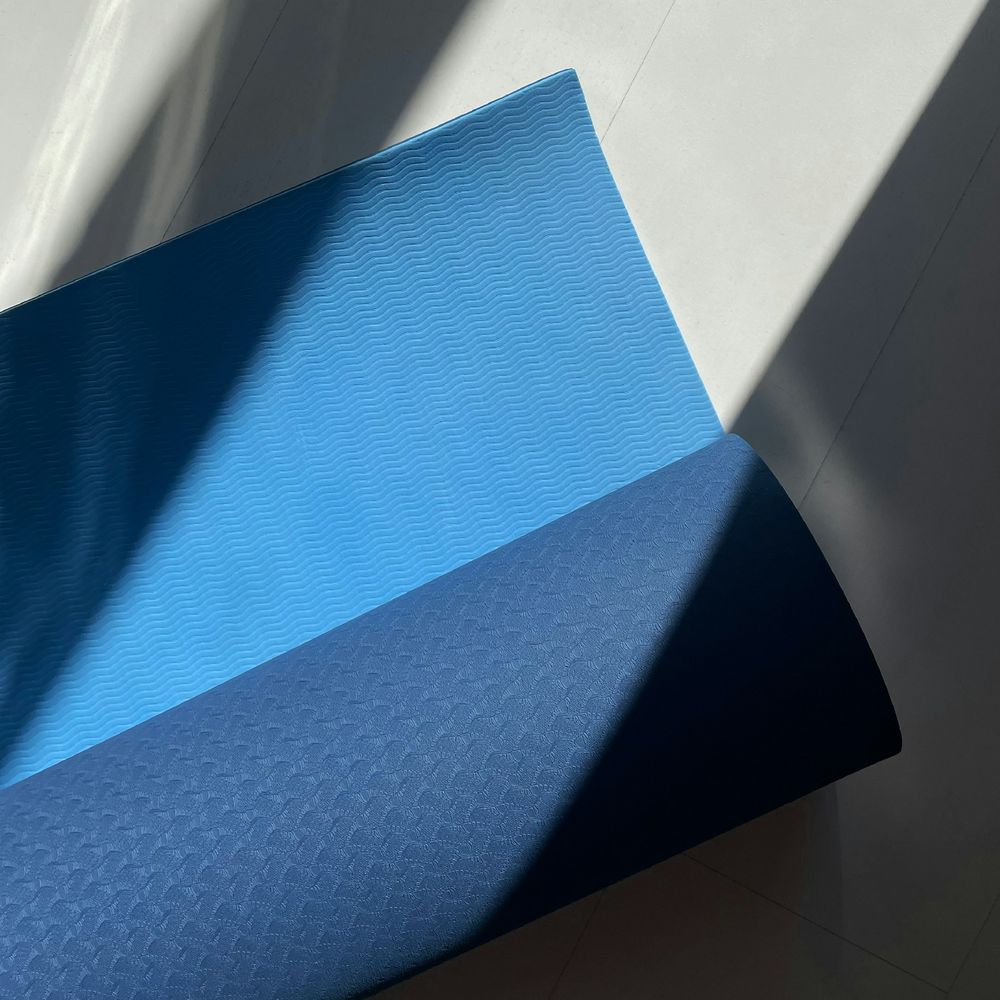 Blue yoga mat with one corner curled over showing a darker underside in strong sunlight