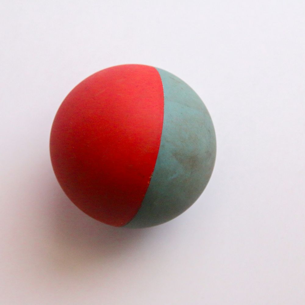 Solid rubber ball, half red and half slate grey, on a pale background