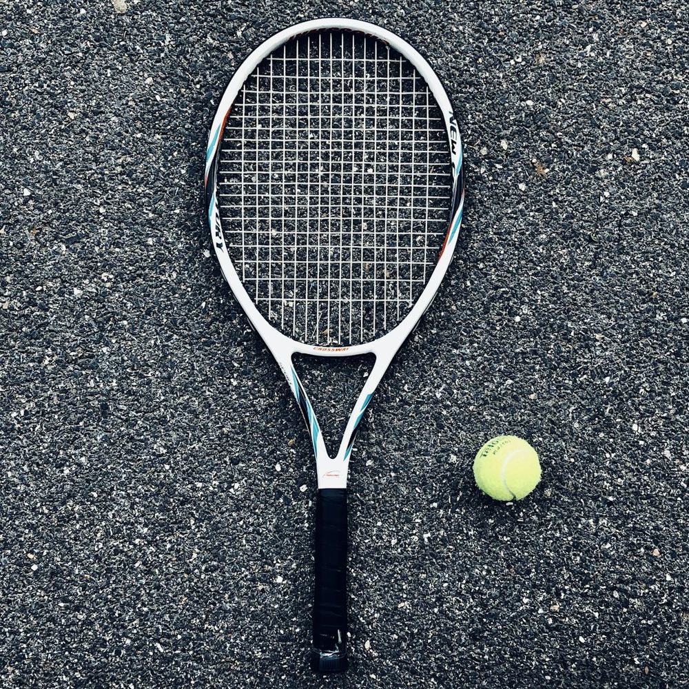 White-framed tennis racket lying on a dark court surface next to a yellow tennis ball